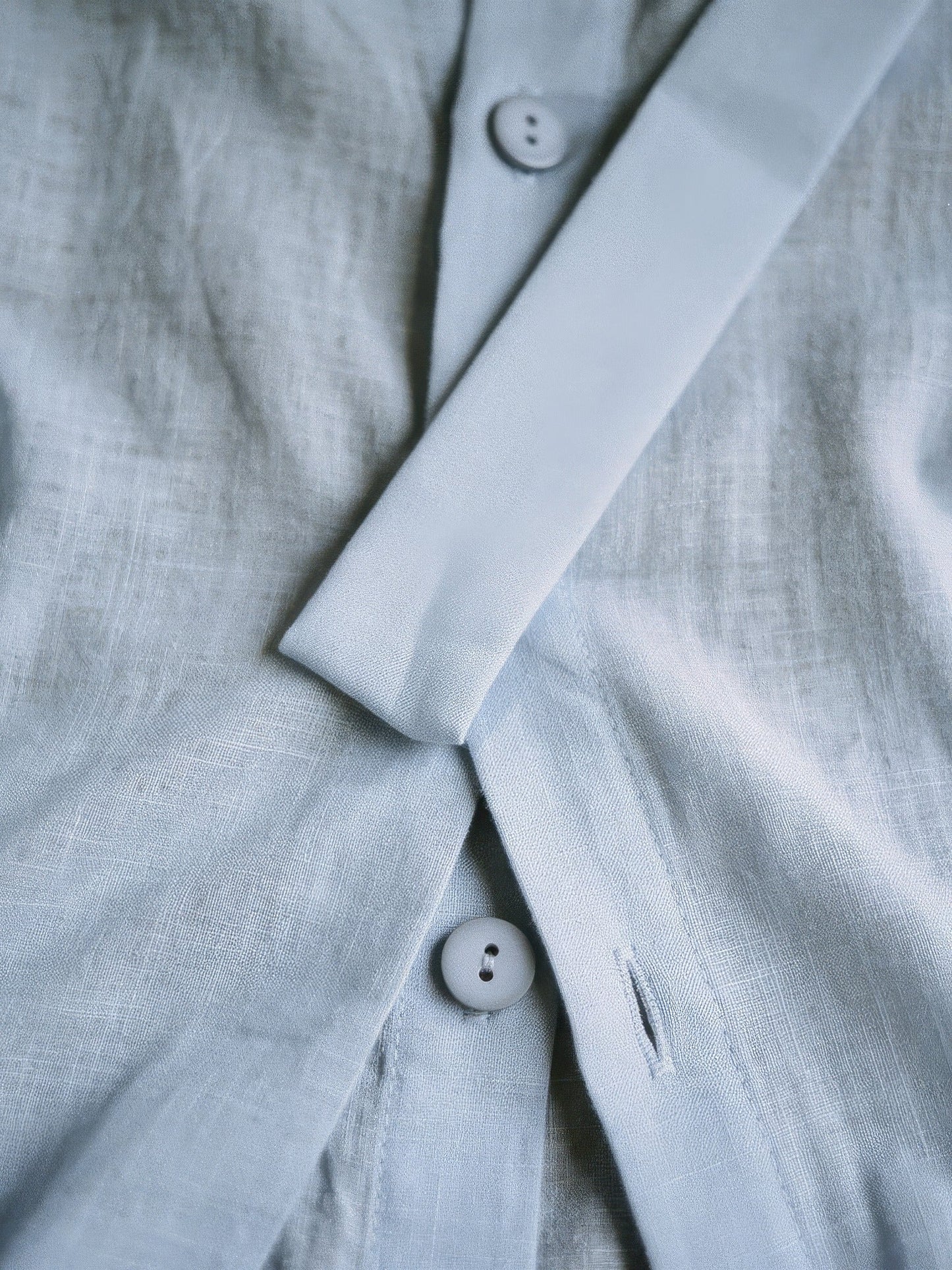 Close up of the powder blue woven fabric, matte slub weave, button and ribbon sash