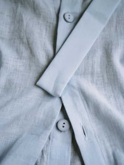 Close up of the powder blue woven fabric, matte slub weave, button and ribbon sash