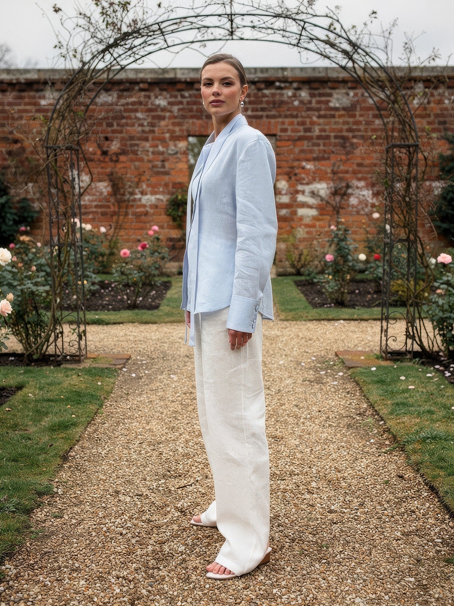 Powder blue tie-waist blouse worn open with the ribbon sash loose, full length, in an English rose garden