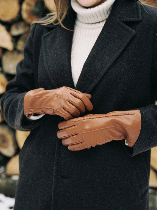 Woman easing on cognac touch screen gloves in fleece lined faux leather