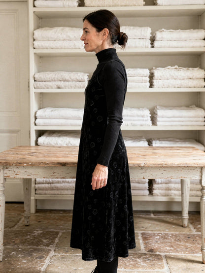 Black velvet slip dress worn over a fine roll neck in a country house linen room