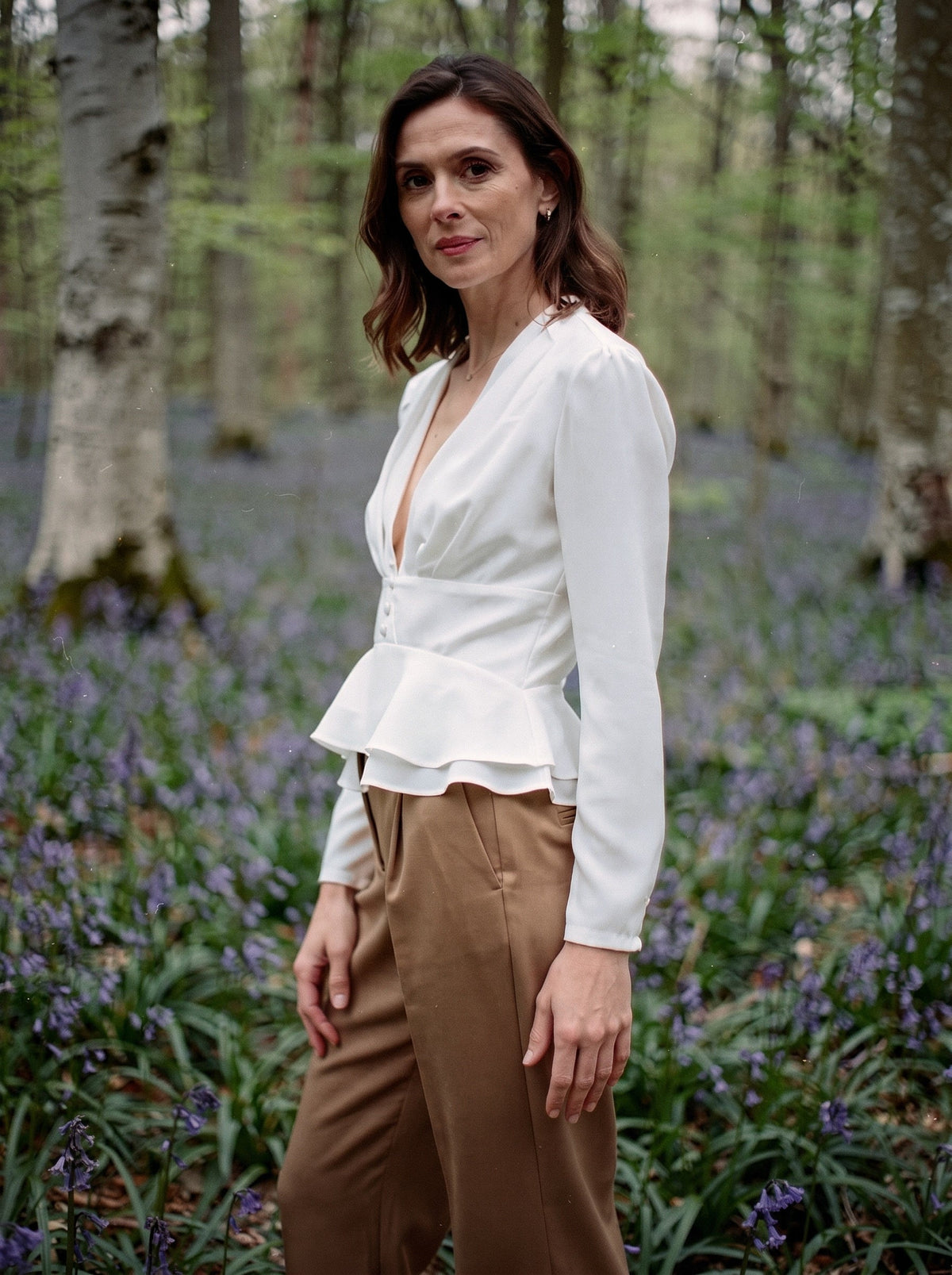 Woman wearing the white peplum blouse with camel trousers in an English bluebell wood