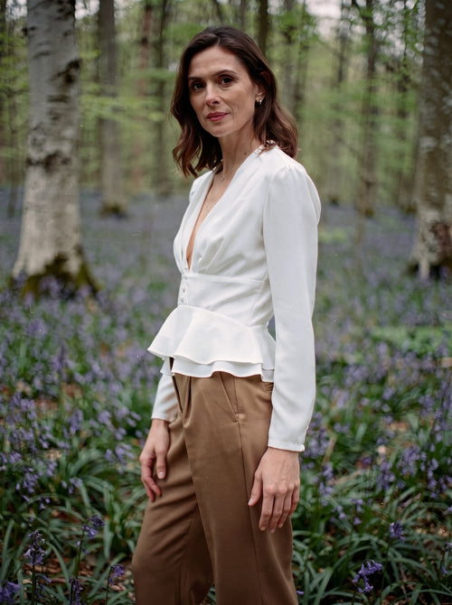 Woman wearing the white peplum blouse with camel trousers in an English bluebell wood