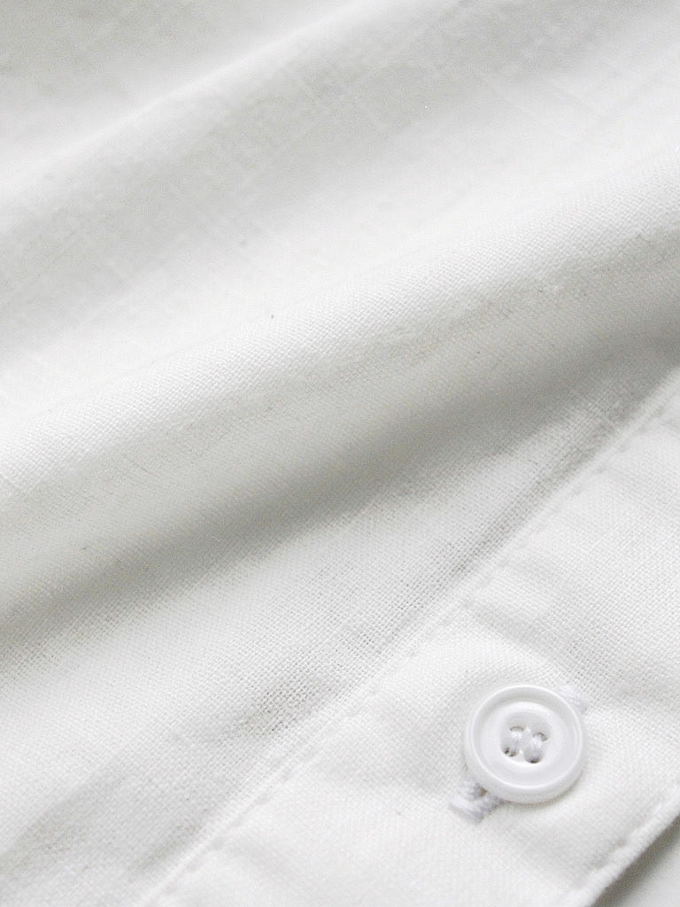 Close up of the soft cotton weave and one white four hole button of the white shirt