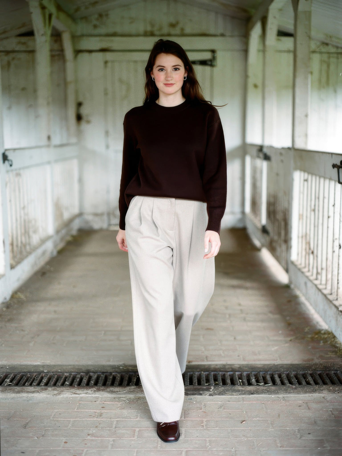 Woman wearing putty wide-leg trousers with a curved barrel leg, walking through a whitewashed English byre