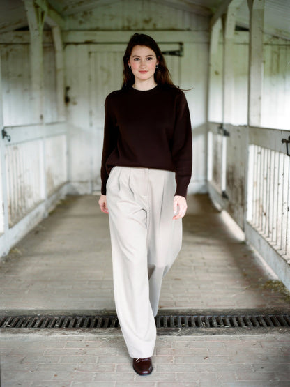 Woman wearing putty wide-leg trousers with a curved barrel leg, walking through a whitewashed English byre