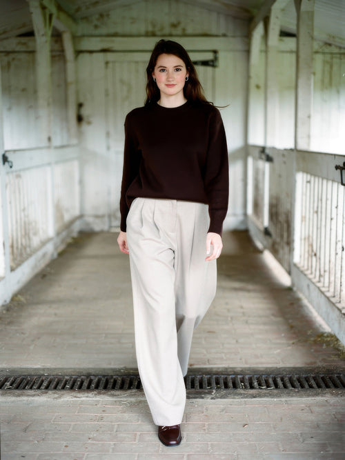 Woman wearing putty wide-leg trousers with a curved barrel leg, walking through a whitewashed English byre