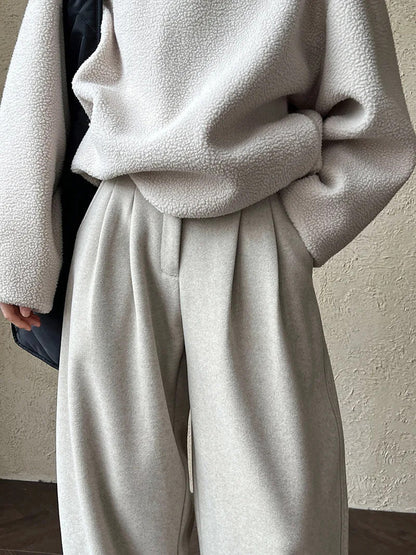 Detail of the flat waistband and soft front pleats of the putty wide-leg trousers