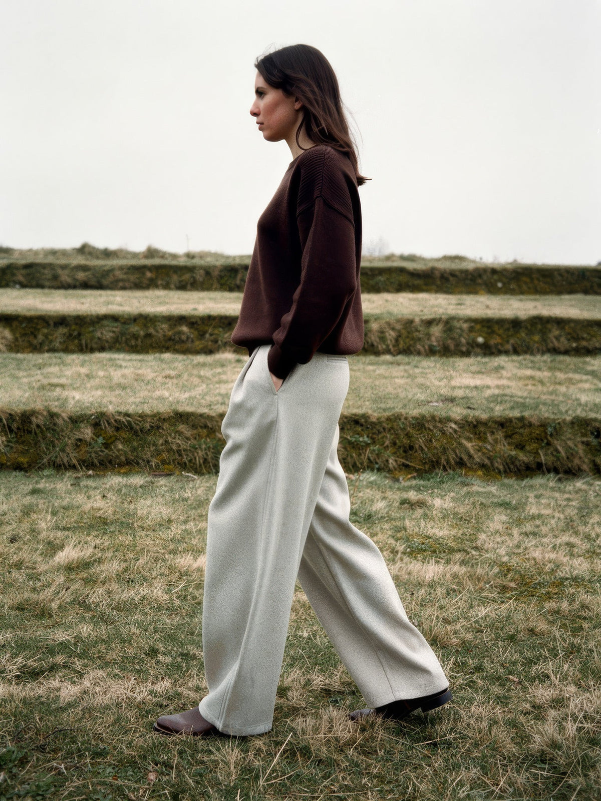 Side profile of putty wide-leg trousers showing the curved barrel leg and full length hem