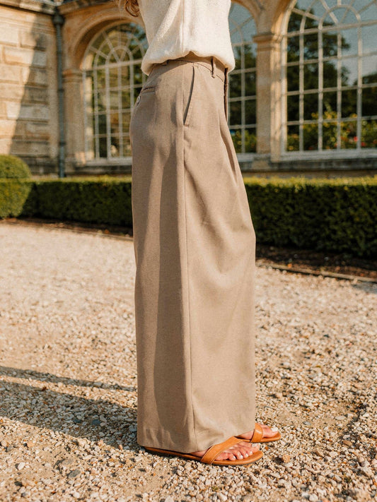 Woman wearing the Winsley high-rise wide-leg trousers in taupe beside a Georgian orangery