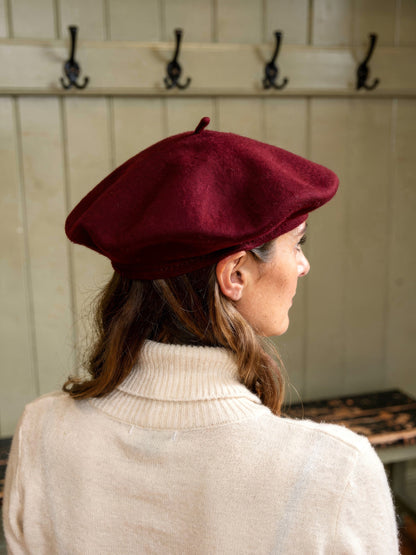 Back view of a womens wine red felt beret hat and its topknot