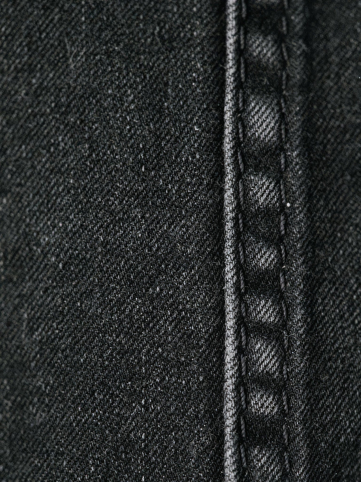 Close-up of the rigid cotton denim and tonal black stitching on the black jeans