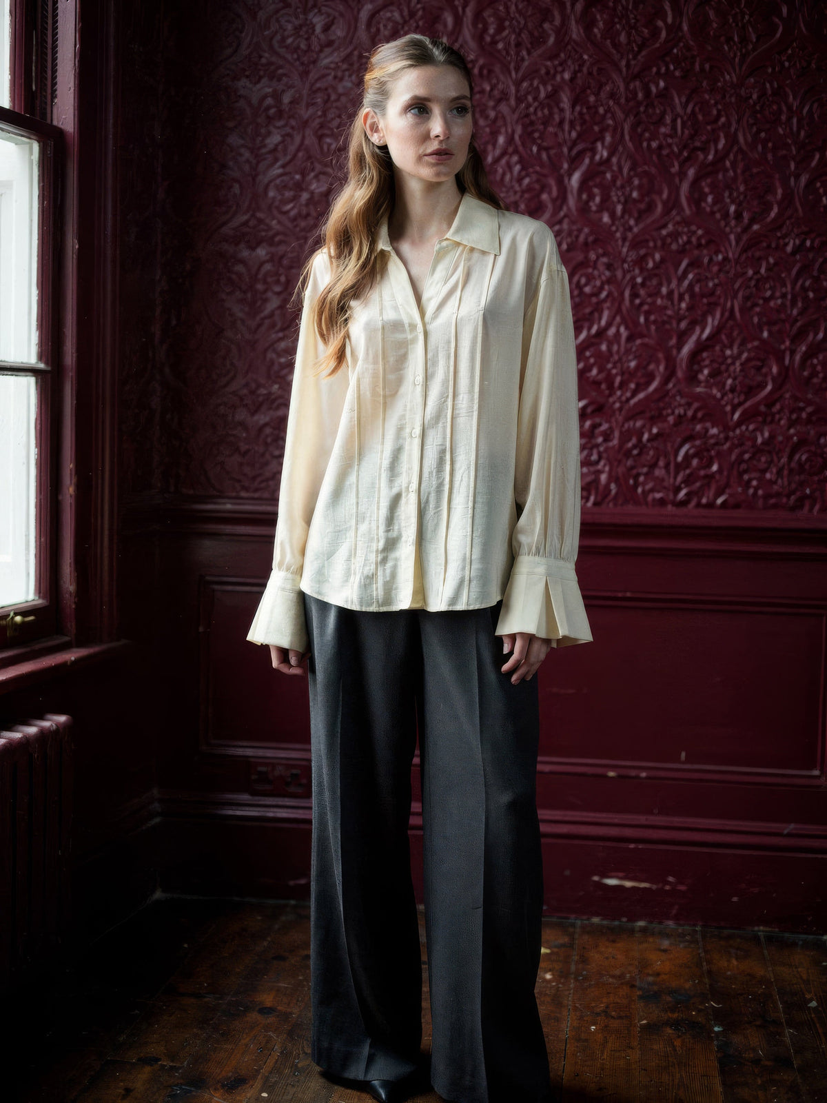 Womens cream blouse with a pintuck front and deep fluted cuffs, worn with charcoal wide leg trousers
