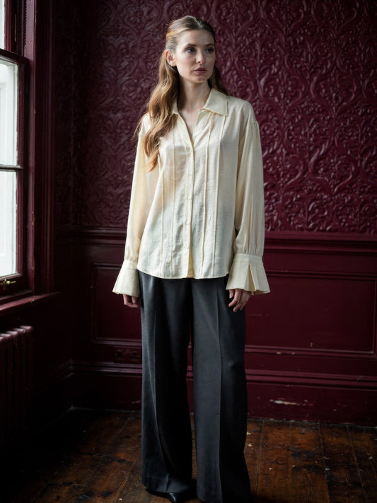 Womens cream blouse with a pintuck front and deep fluted cuffs, worn with charcoal wide leg trousers