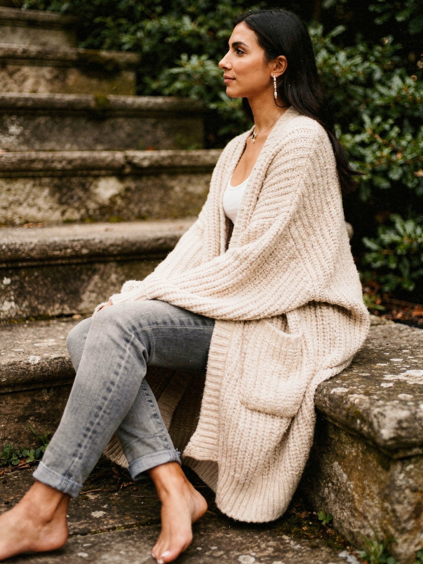 Woman in an oatmeal longline chunky rib cardigan seated on stone steps