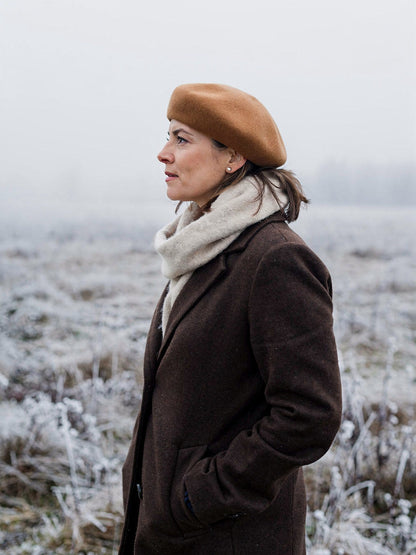 Side profile of a woman wearing a gingerbread wool beret on a frosted winter meadow