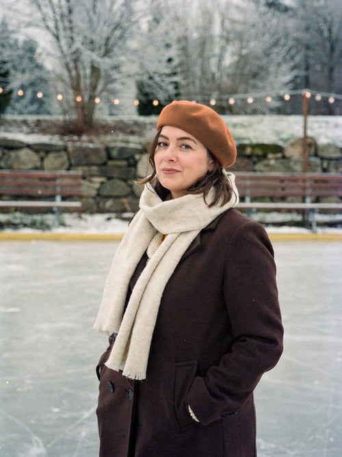 Woman wearing a gingerbread wool beret beside a frozen outdoor ice rink