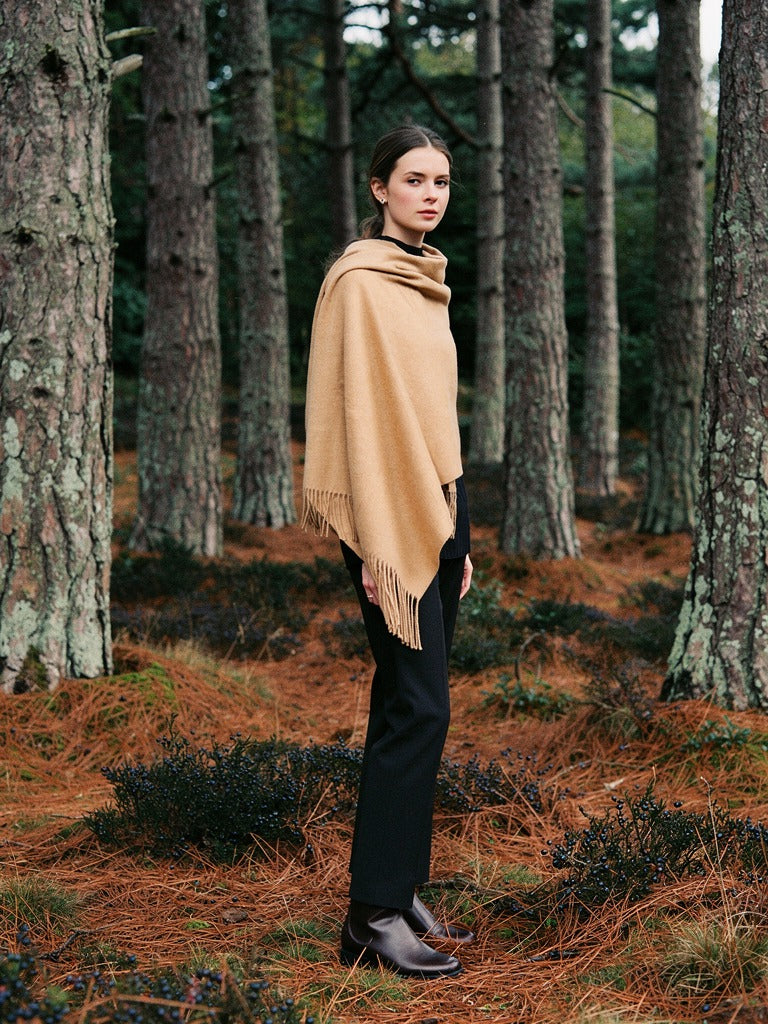 Woman wearing the camel wool pashmina shawl draped over both shoulders in a stand of Scots pines