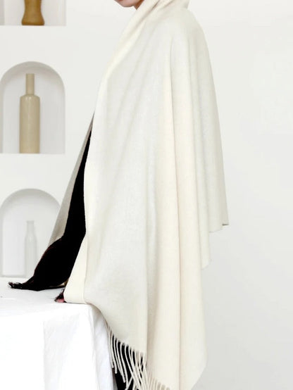 The chalk wool pashmina shawl worn open over both shoulders, showing its full width and tassels