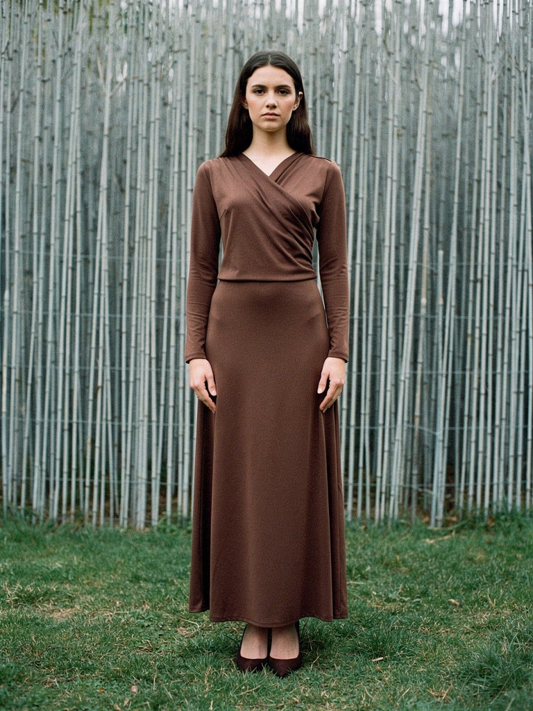 Wrap dress in cherrywood brown worn full length against a pale silvery screen of cut rods