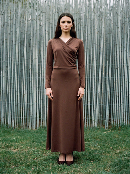 Wrap dress in cherrywood brown worn full length against a pale silvery screen of cut rods