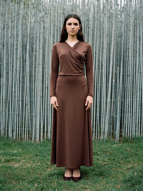 Wrap dress in cherrywood brown worn full length against a pale silvery screen of cut rods